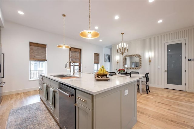 kitchen featuring stainless steel dishwasher, hanging light fixtures, a sink, light wood-style floors, and gray cabinetry