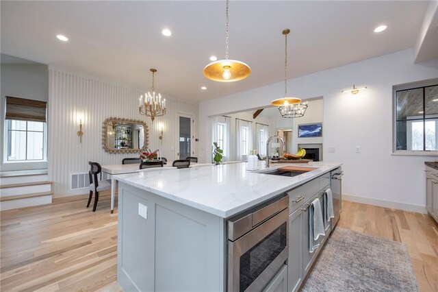 kitchen featuring a sink, stainless steel microwave, light wood-style floors, a chandelier, and a fireplace