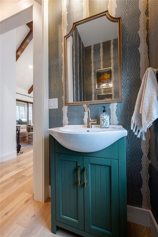 bathroom featuring baseboards, vanity, wood finished floors, and beamed ceiling