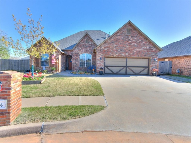 view of front of home featuring a front yard, fence, brick siding, an attached garage, and concrete driveway