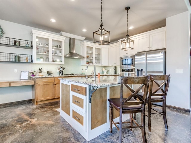 kitchen featuring wall chimney exhaust hood, a breakfast bar, a sink, stainless steel appliances, and a center island with sink