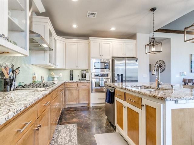 kitchen featuring glass insert cabinets, a sink, appliances with stainless steel finishes, a center island with sink, and backsplash