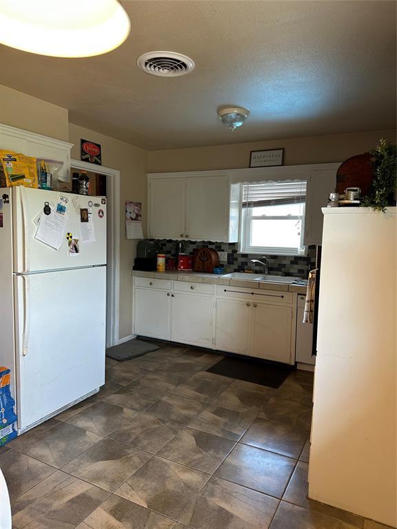 609 Utah Ave, Norman, OK 73069 - kitchen with visible vents, white cabinets, a sink, freestanding refrigerator, and decorative backsplash