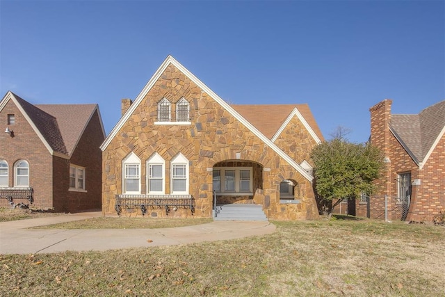 english style home with a chimney, a front yard, and stone siding