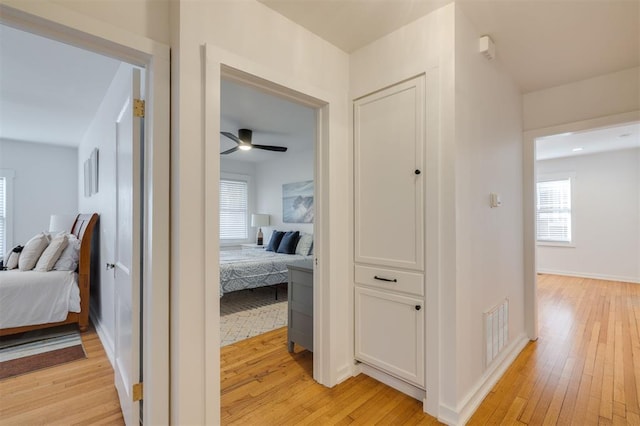 corridor featuring visible vents, baseboards, and light wood-style flooring