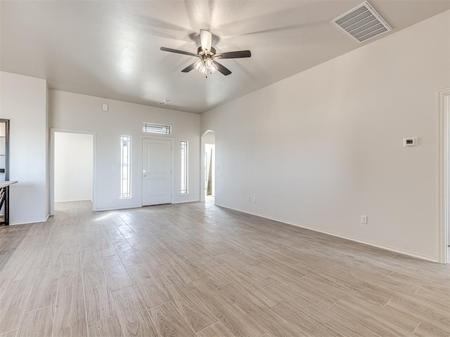 unfurnished living room with visible vents, baseboards, arched walkways, ceiling fan, and light wood-style flooring