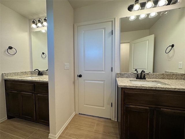 bathroom with a sink, two vanities, wood finish floors, and baseboards
