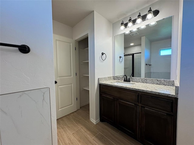 bathroom with vanity, baseboards, wood finish floors, a shower stall, and visible vents