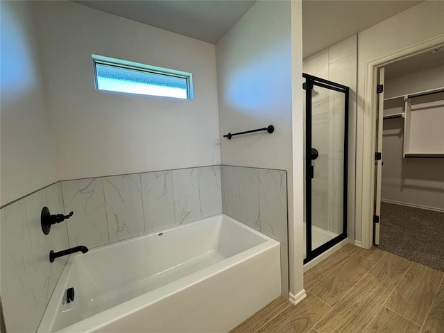 full bathroom featuring a shower stall, a bath, a walk in closet, and wood tiled floor