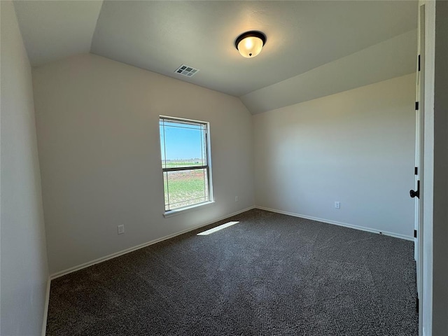 spare room featuring dark carpet, visible vents, baseboards, and lofted ceiling