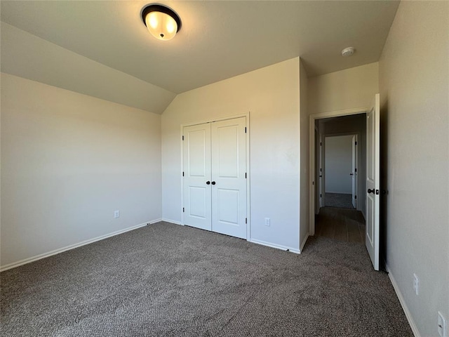 unfurnished bedroom with baseboards, a closet, dark colored carpet, and lofted ceiling