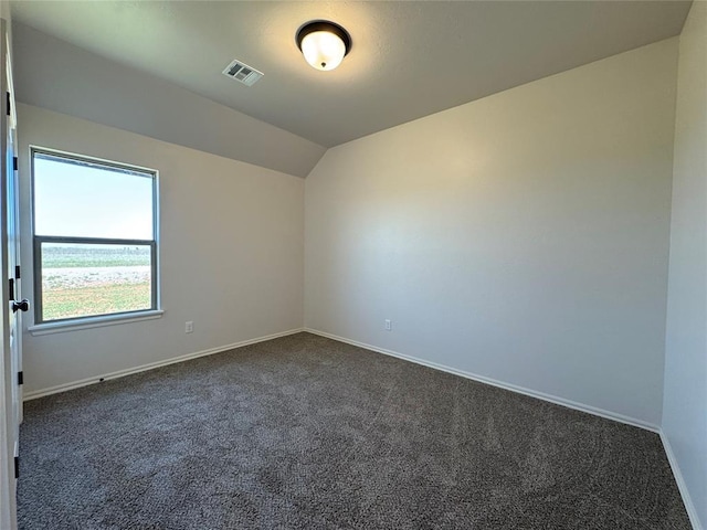 spare room with dark carpet, baseboards, lofted ceiling, and visible vents