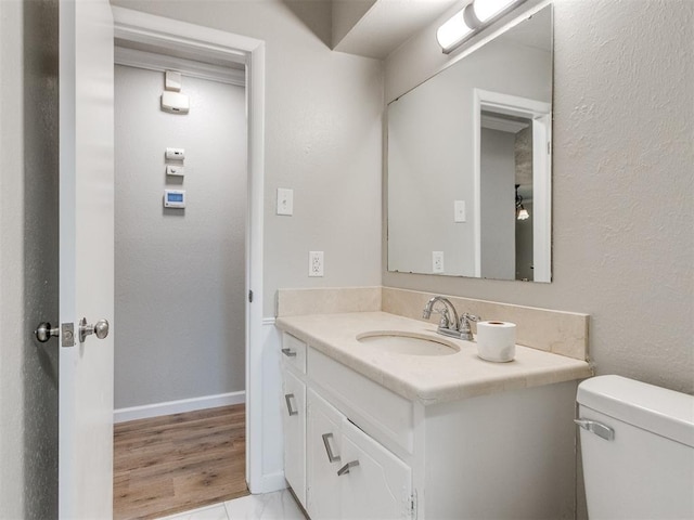 bathroom with a textured wall, toilet, vanity, and baseboards