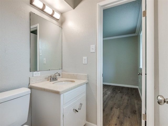 bathroom featuring baseboards, toilet, crown molding, vanity, and wood finished floors