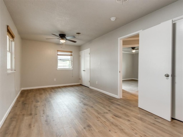 spare room with baseboards, a ceiling fan, light wood-style floors, and a textured ceiling