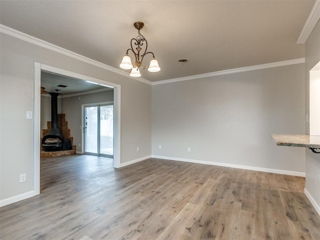 unfurnished dining area with baseboards, an inviting chandelier, ornamental molding, a wood stove, and wood finished floors