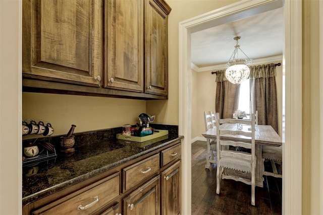 interior space featuring dark stone counters, dark wood-style flooring, a notable chandelier, baseboards, and ornamental molding