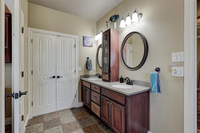 full bath with stone finish flooring, baseboards, a sink, and double vanity