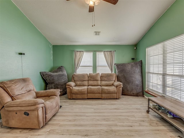 living area with visible vents, light wood-style flooring, a ceiling fan, and lofted ceiling