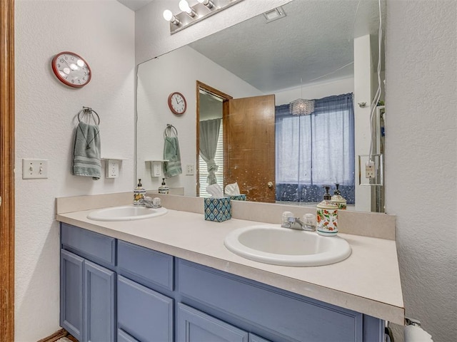 full bath featuring a textured wall, double vanity, a textured ceiling, and a sink