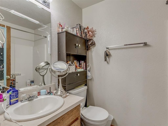 full bathroom with toilet, vanity, and a textured wall