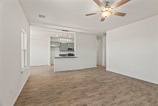 unfurnished living room with baseboards, wood finished floors, visible vents, and ceiling fan