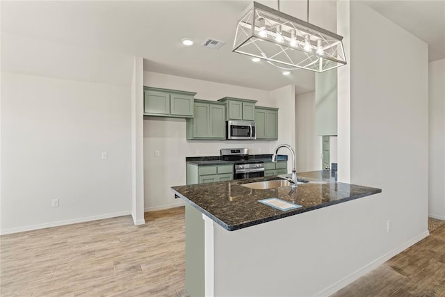 kitchen with stainless steel appliances, visible vents, a sink, light wood-type flooring, and green cabinets