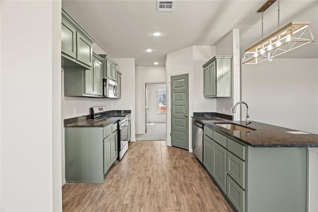 kitchen with a sink, stainless steel appliances, a peninsula, green cabinetry, and visible vents