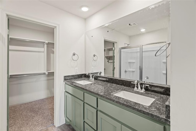 full bath featuring a walk in closet, double vanity, a shower stall, and a sink