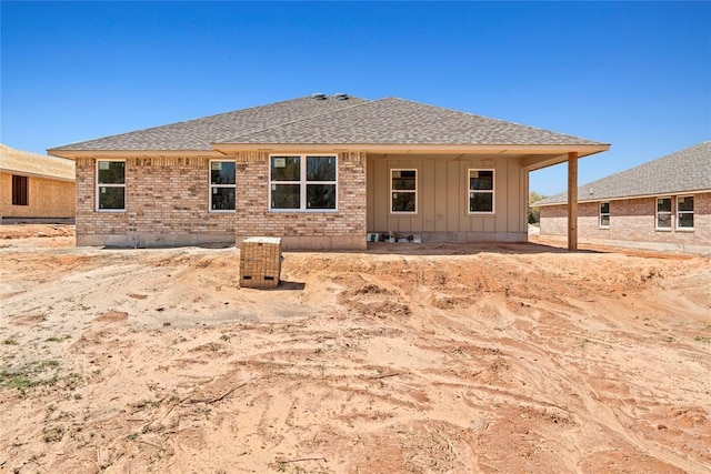 back of property with board and batten siding, brick siding, and a shingled roof