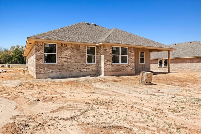 rear view of property featuring a shingled roof and brick siding