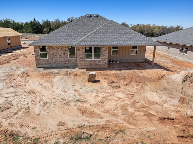 back of house with board and batten siding, roof with shingles, and brick siding