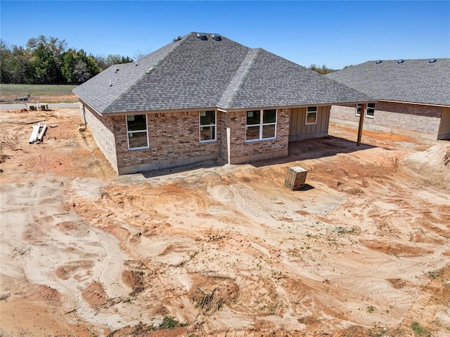 back of house with brick siding, roof with shingles, and board and batten siding
