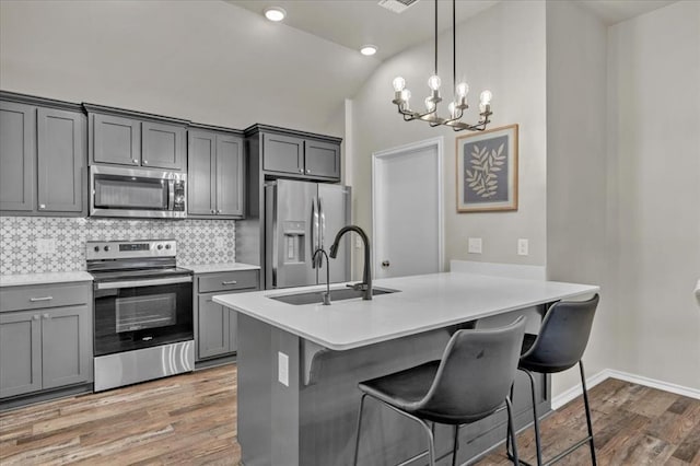 kitchen featuring stainless steel appliances, vaulted ceiling, wood finished floors, a kitchen bar, and a notable chandelier