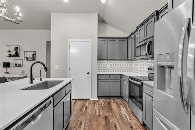 kitchen featuring lofted ceiling, hardwood / wood-style floors, light countertops, a sink, and appliances with stainless steel finishes