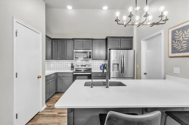 kitchen with an inviting chandelier, a sink, gray cabinetry, a kitchen bar, and appliances with stainless steel finishes