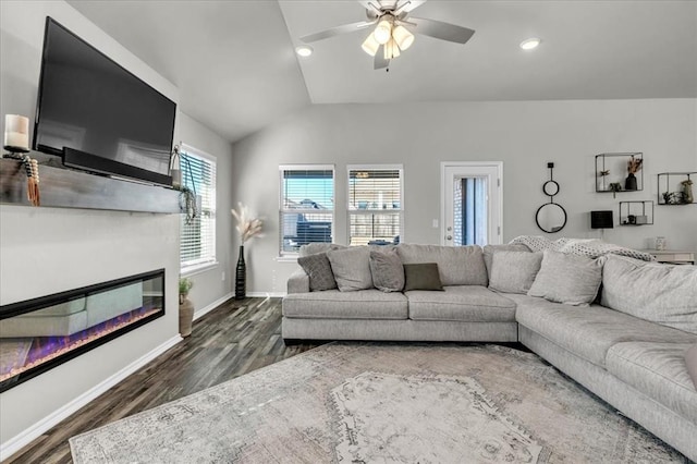 living room with vaulted ceiling, a glass covered fireplace, ceiling fan, baseboards, and dark wood-type flooring
