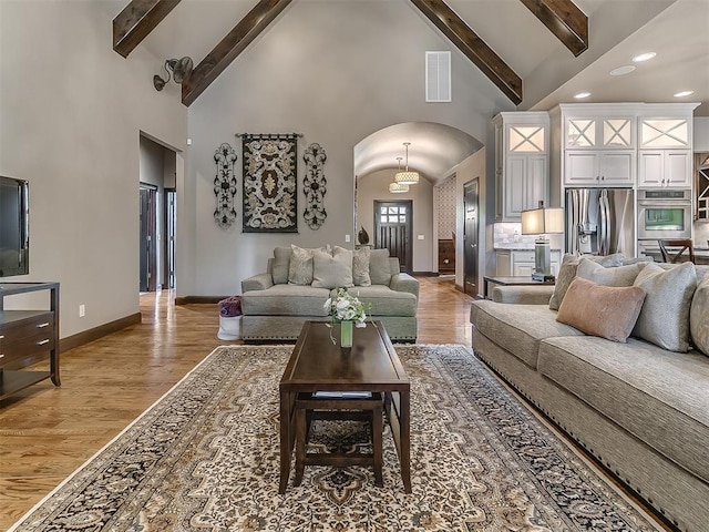 living area with visible vents, wood finished floors, beamed ceiling, high vaulted ceiling, and arched walkways