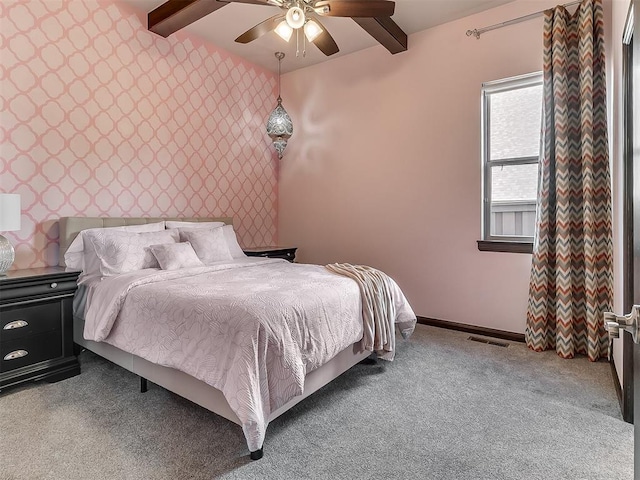 carpeted bedroom featuring a ceiling fan, beamed ceiling, an accent wall, and wallpapered walls