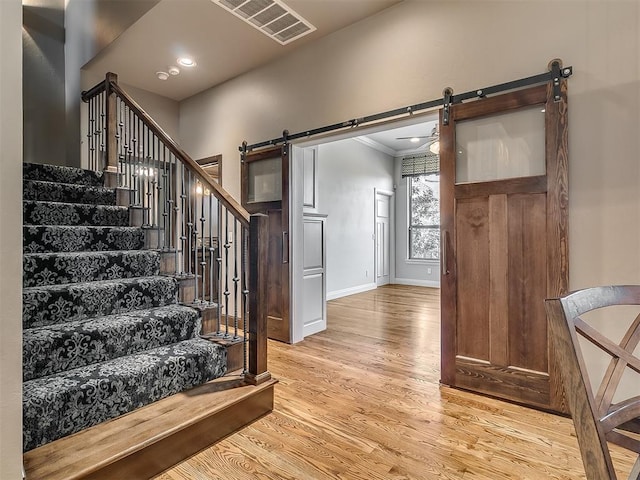 stairs with a barn door, baseboards, wood finished floors, visible vents, and ornamental molding