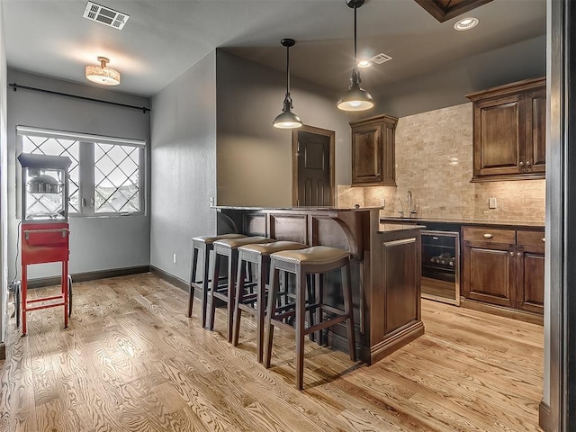 bar featuring visible vents, decorative backsplash, wine cooler, light wood-style flooring, and hanging light fixtures