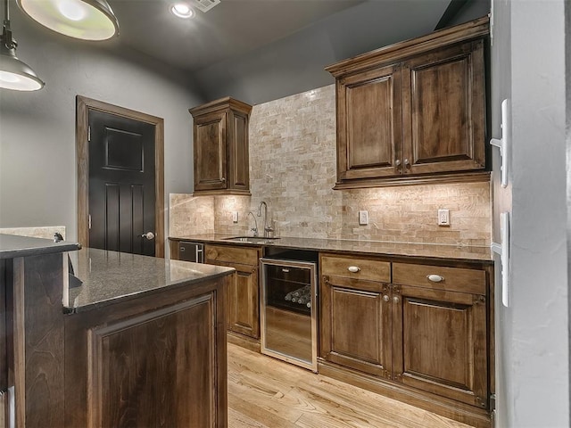 kitchen featuring a sink, beverage cooler, dark stone countertops, light wood-type flooring, and backsplash