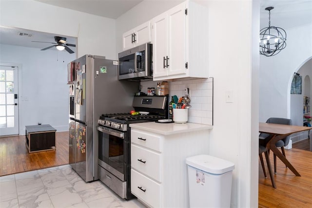 1428 NW 45th St, Oklahoma City, OK 73118 - kitchen featuring stainless steel appliances, arched walkways, tasteful backsplash, ceiling fan with notable chandelier, and light countertops