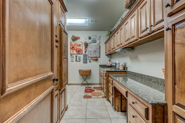 3615 S Scissortail Dr, Stillwater, OK 74074 - interior space with light tile patterned floors, brown cabinetry, dark stone countertops, a sink, and baseboards