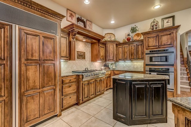 3615 S Scissortail Dr, Stillwater, OK 74074 - kitchen featuring tasteful backsplash, dark stone countertops, a center island, brown cabinets, and appliances with stainless steel finishes