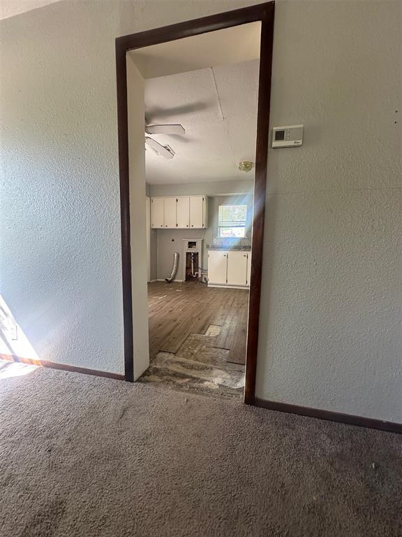 hallway featuring baseboards, a textured wall, and dark colored carpet