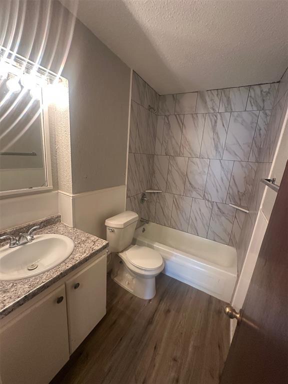 full bath with a textured ceiling,  shower combination, toilet, wood finished floors, and vanity