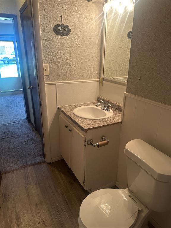 half bath featuring a textured wall, a decorative wall, wood finished floors, and wainscoting
