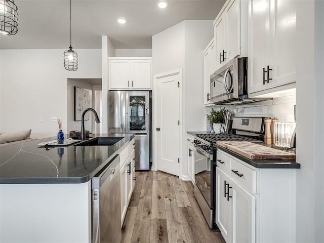 kitchen featuring light wood-style flooring, white cabinetry, dark countertops, stainless steel appliances, and decorative backsplash