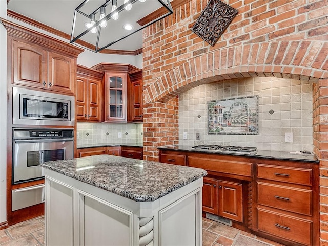 1217 Camelot Dr, Yukon, OK 73099 - kitchen featuring stainless steel appliances, dark stone countertops, a warming drawer, stone tile floors, and ornamental molding